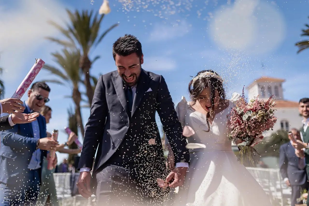 Pareja de novios siendo rociados por arroz durante la celebración de su boda en Finca el Jardín de la Estación.